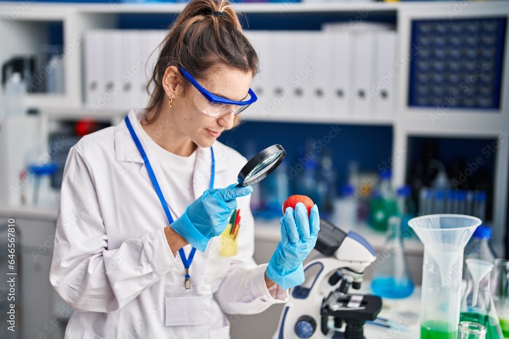 Young woman scientist looking fruit with loupe at laboratory