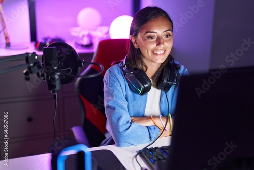 Young beautiful hispanic woman streamer smiling confident sitting with arms crossed gesture at gaming room