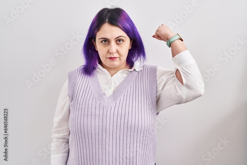 Plus size woman wit purple hair standing over white background strong person showing arm muscle, confident and proud of power © Krakenimages.com