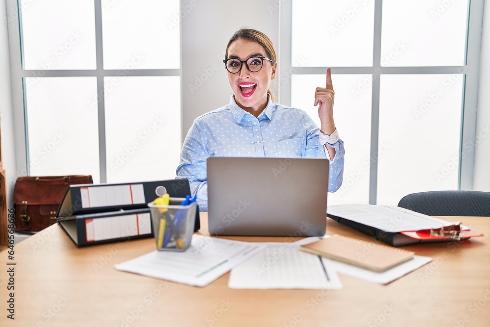 Young hispanic woman working at the office wearing glasses pointing finger up with successful idea. exited and happy. number one. Young hispanic woman working at the office wearing glasses pointing finger up with successful idea. exited and happy. number one.