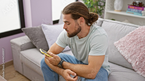 Young hispanic man using smartphone sitting on sofa thinking at home