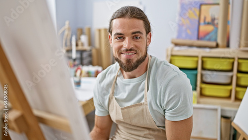 Young hispanic man artist smiling confident sitting on chair at art studio