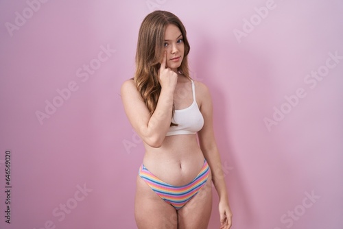 Caucasian woman wearing lingerie over pink background pointing to the eye watching you gesture, suspicious expression
