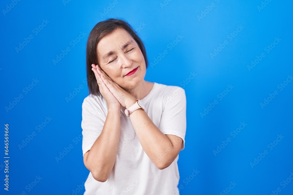 Middle age hispanic woman standing over blue background sleeping tired dreaming and posing with hands together while smiling with closed eyes. Middle age hispanic woman standing over blue background sleeping tired dreaming and posing with hands together while smiling with closed eyes.