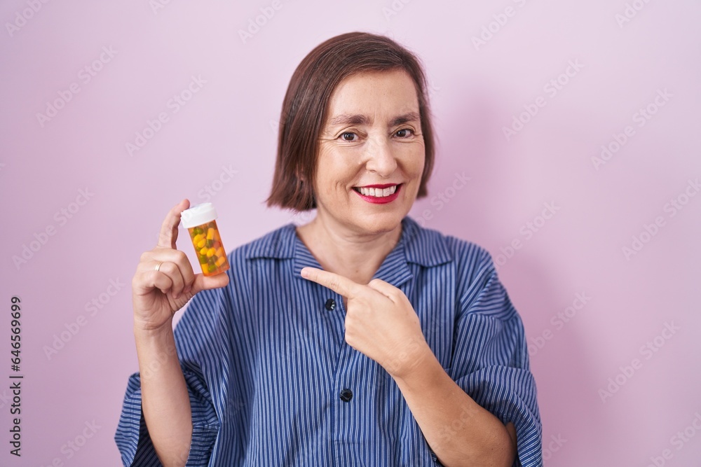 Middle age hispanic woman holding pills smiling happy pointing with hand and finger Middle age hispanic woman holding pills smiling happy pointing with hand and finger