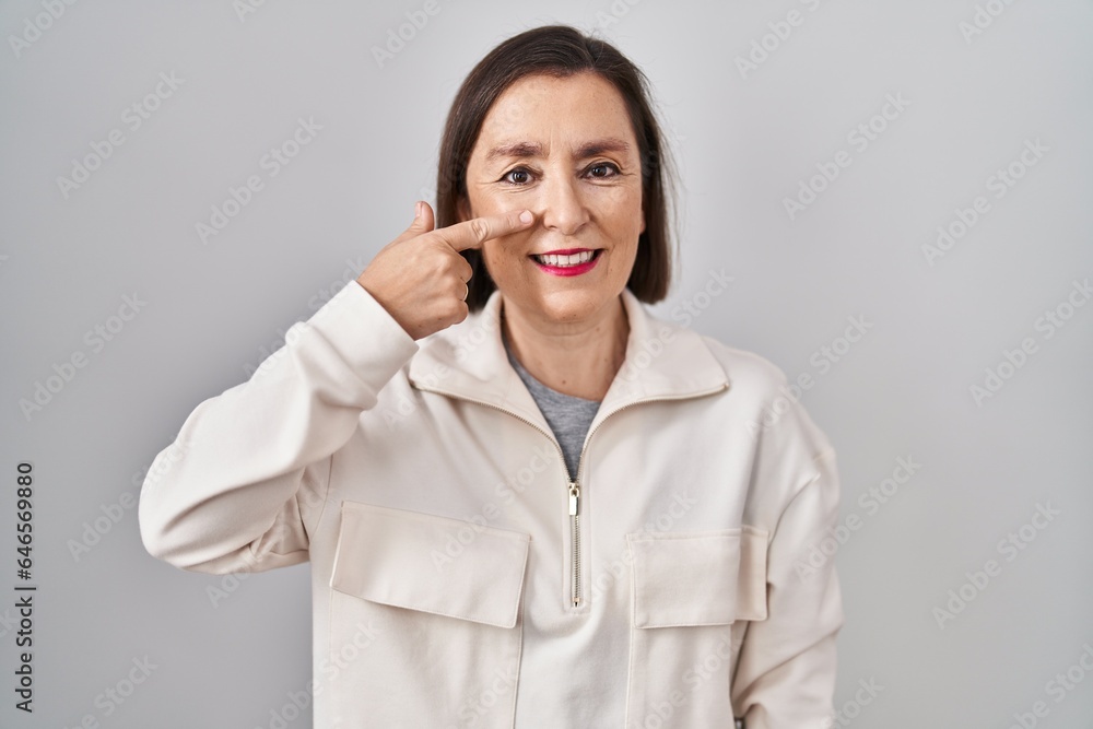 Middle age hispanic woman standing over isolated background pointing with hand finger to face and nose, smiling cheerful. beauty concept Middle age hispanic woman standing over isolated background pointing with hand finger to face and nose, smiling cheerful. beauty concept