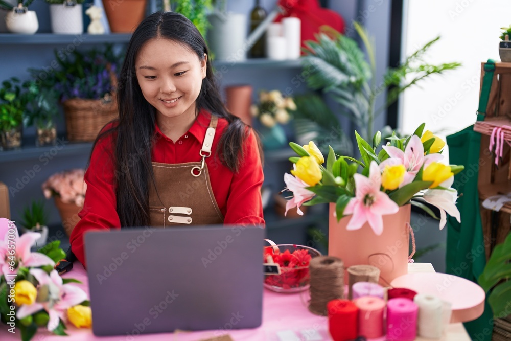 Young chinese woman florist smiling confident using laptop at flower shop
