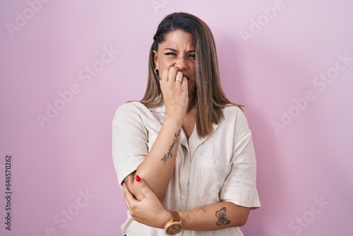 Blonde woman standing over pink background looking stressed and nervous with hands on mouth biting nails. anxiety problem.