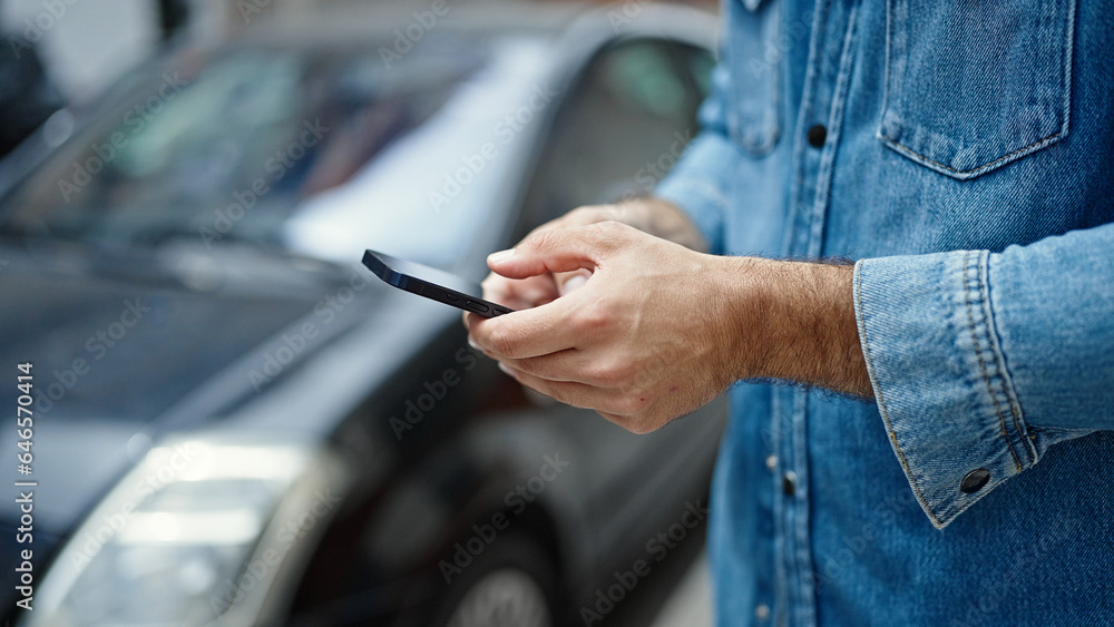 Young hispanic man using smartphone standing by car at street