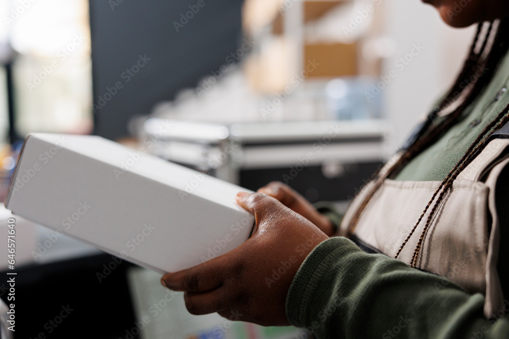 Stockroom worker holding white carton box, preparing packages for shipping in warehouse. Storage room worker wearing industrial overall working at customers orders in storehouse