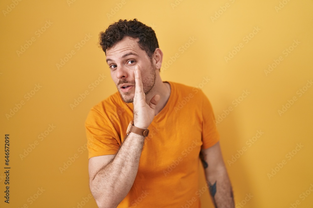 Young hispanic man standing over yellow background hand on mouth telling secret rumor, whispering malicious talk conversation Young hispanic man standing over yellow background hand on mouth telling secret rumor, whispering malicious talk conversation