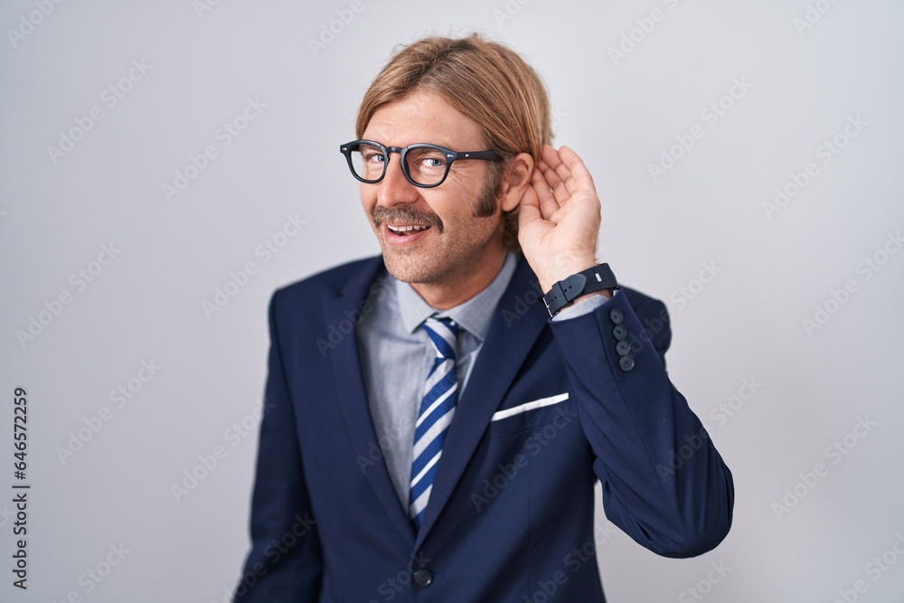 Caucasian man with mustache wearing business clothes smiling with hand over ear listening an hearing to rumor or gossip. deafness concept. Caucasian man with mustache wearing business clothes smiling with hand over ear listening an hearing to rumor or gossip. deafness concept.
