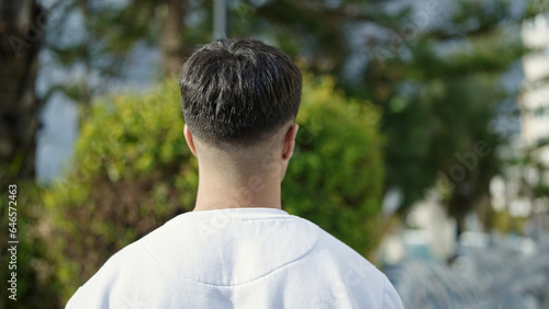 Young hispanic man standing backwards at park