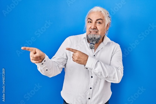 Middle age man with grey hair standing over blue background pointing aside worried and nervous with both hands, concerned and surprised expression © Krakenimages.com