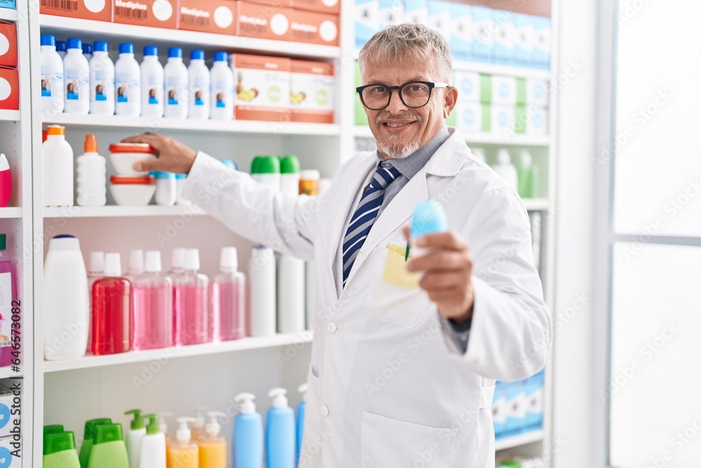 Middle age grey-haired man pharmacist holding deodorant bottle at laboratory