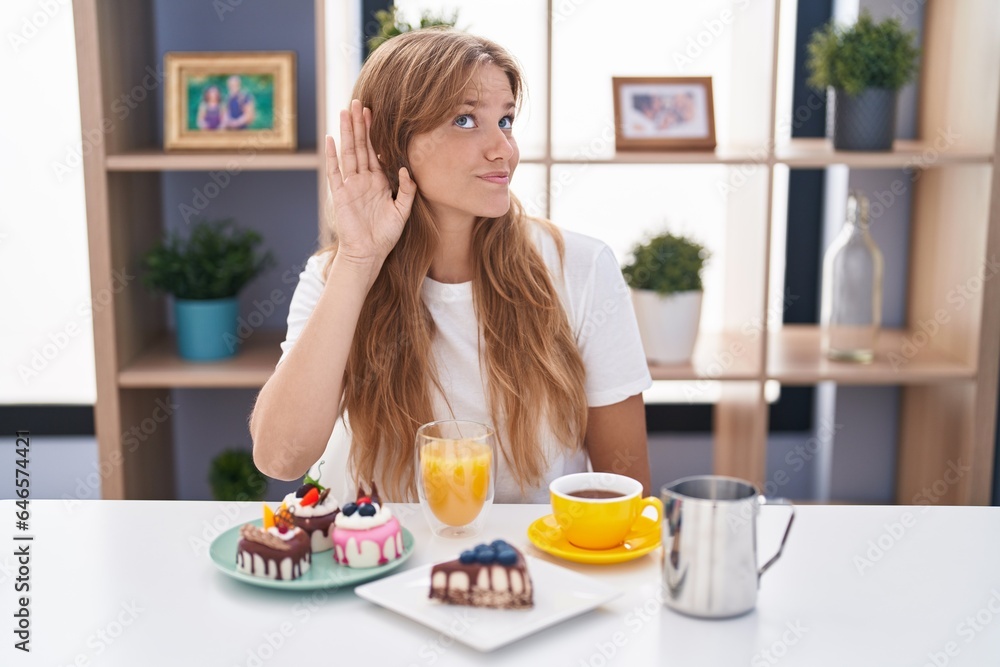 Young caucasian woman eating pastries t for breakfast smiling with hand over ear listening an hearing to rumor or gossip. deafness concept.