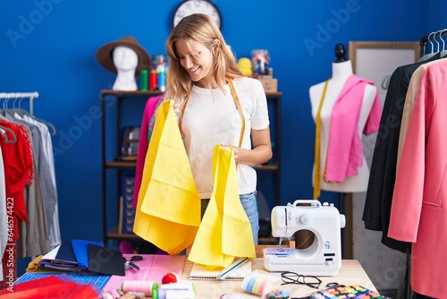 Young blonde girl tailor smiling confident holding cloths at sewing studio