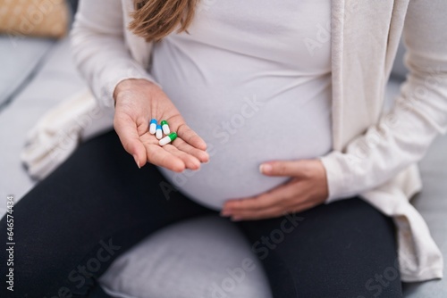 Young pregnant woman touching belly holding pills at home