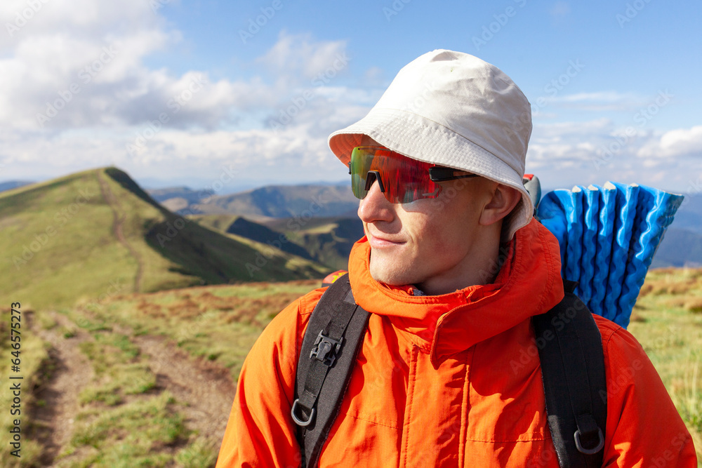 man in jacket and sunglasses stands on the mountain and looks at the sun, tourist guy in mountain clothes man in jacket and sunglasses stands on the mountain and looks at the sun, tourist guy in mountain clothes