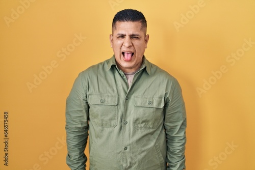 Hispanic young man standing over yellow background sticking tongue out happy with funny expression. emotion concept. © Krakenimages.com