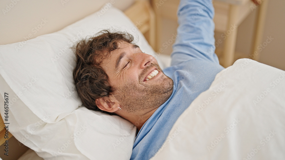 Young hispanic man waking up stretching arms at bedroom Young hispanic man waking up stretching arms at bedroom