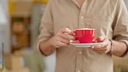 Young hispanic man holding cup of coffee standing at new home
