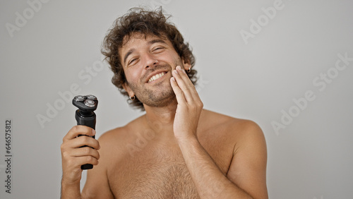 Bilde på lerret Young hispanic man massaging bear holding shaver machine smiling shirtless over
