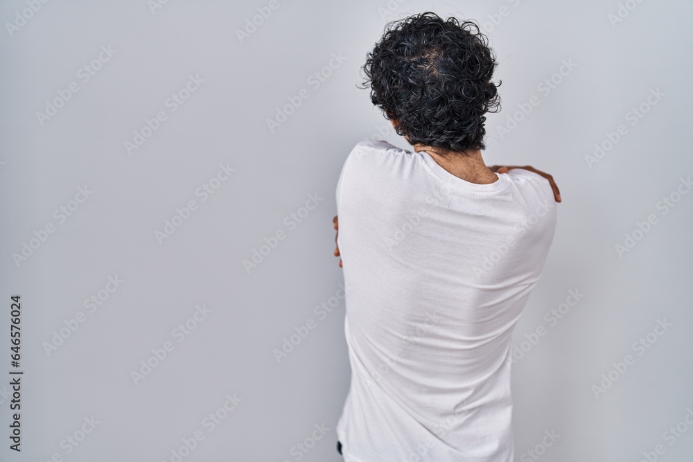 Hispanic man standing over isolated background hugging oneself happy and positive from backwards. self love and self care Hispanic man standing over isolated background hugging oneself happy and positive from backwards. self love and self care