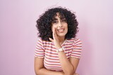 Young middle east woman standing over pink background hand on mouth telling secret rumor, whispering malicious talk conversation