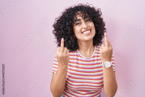 Young middle east woman standing over pink background showing middle finger doing fuck you bad expression, provocation and rude attitude. screaming excited © Krakenimages.com