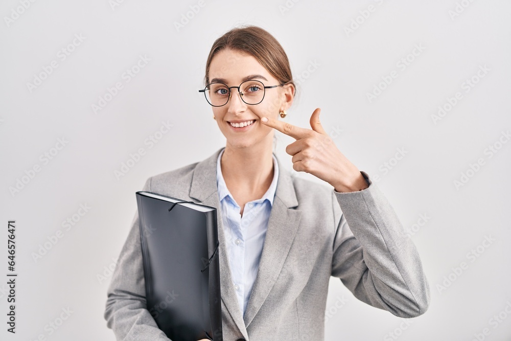 Young caucasian woman wearing business clothes and glasses pointing with hand finger to face and nose, smiling cheerful. beauty concept Young caucasian woman wearing business clothes and glasses pointing with hand finger to face and nose, smiling cheerful. beauty concept