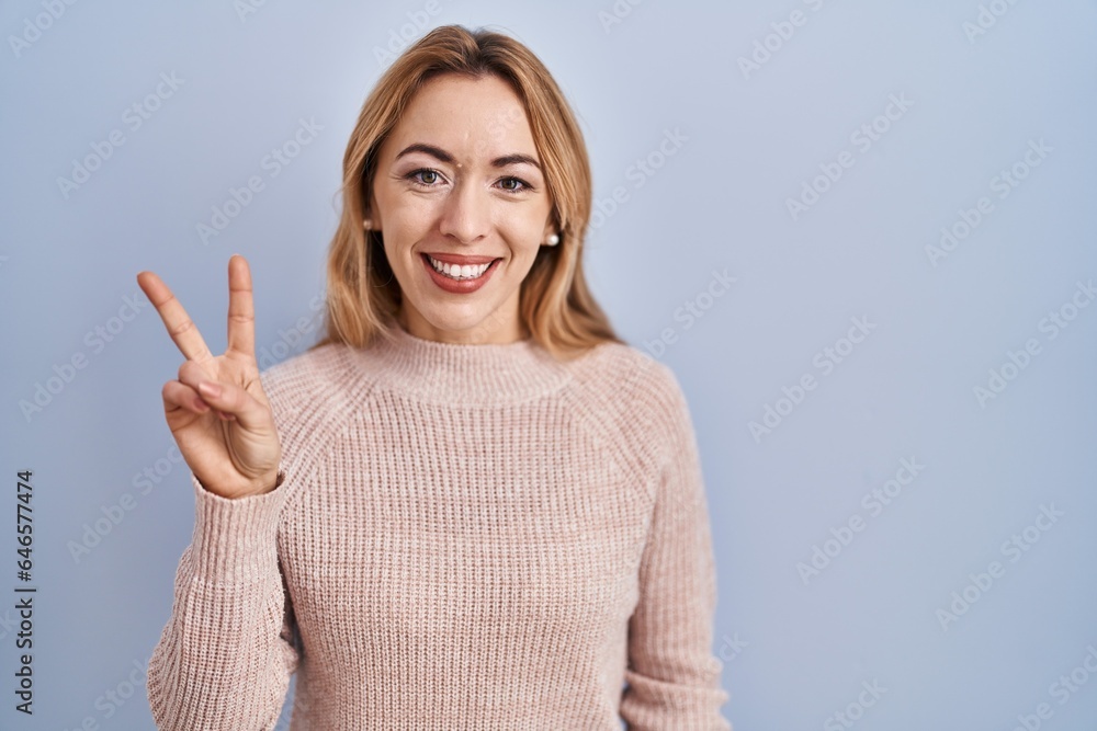 Hispanic woman standing over blue background showing and pointing up with fingers number two while smiling confident and happy. Hispanic woman standing over blue background showing and pointing up with fingers number two while smiling confident and happy.