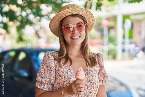 Young woman tourist wearing summer hat eating ice cream at street