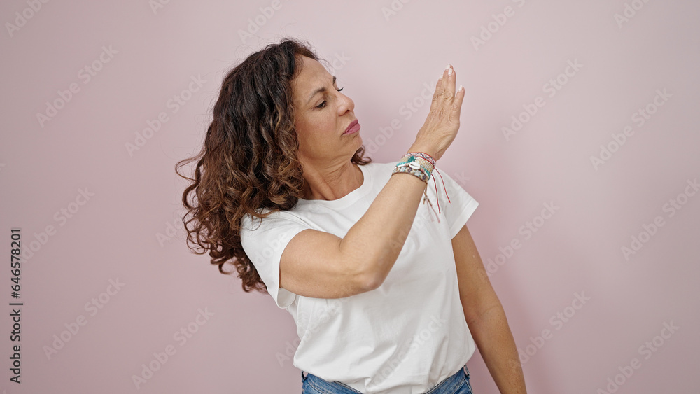 Middle age hispanic woman pointing to blank space with angry face over isolated pink background Middle age hispanic woman pointing to blank space with angry face over isolated pink background