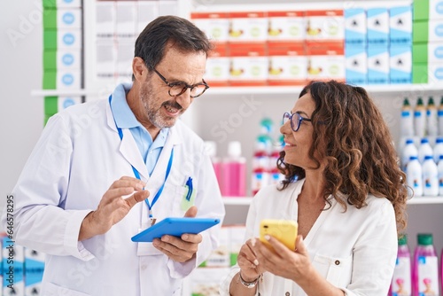 Man and woman pharmacists using touchpad and smartphone working at pharmacy