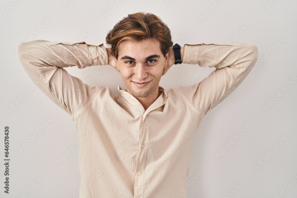Young man standing over isolated background relaxing and stretching, arms and hands behind head and neck smiling happy Young man standing over isolated background relaxing and stretching, arms and hands behind head and neck smiling happy