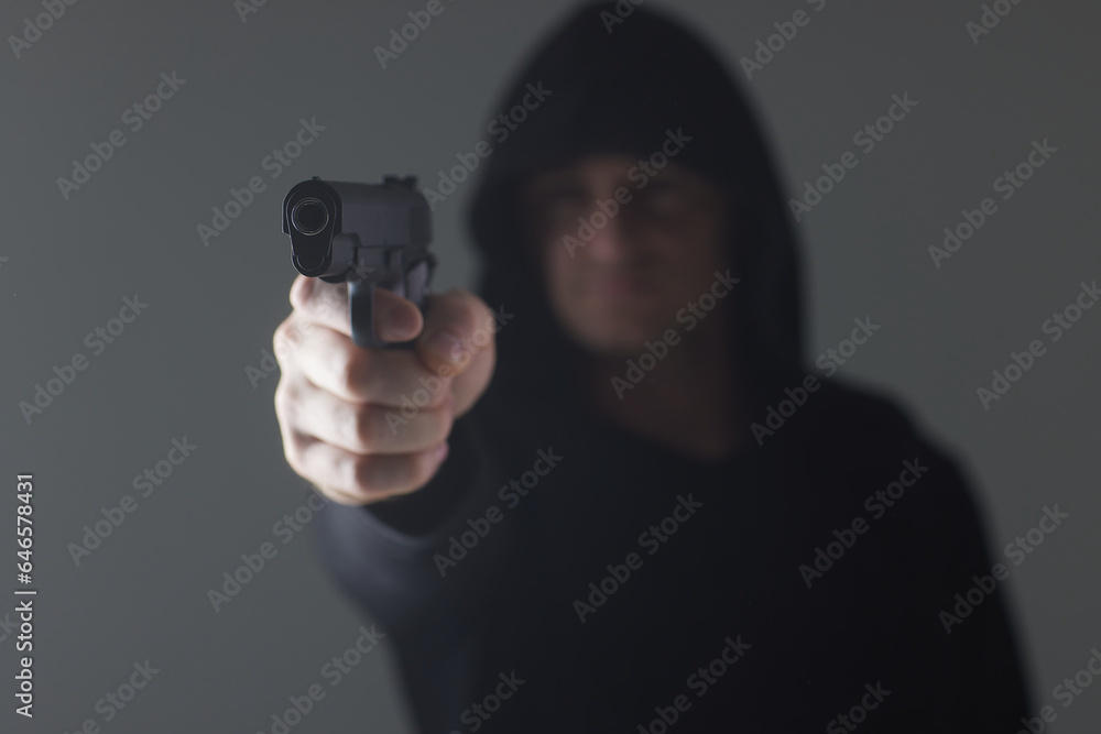 robber with gun aiming into camera. Man in hood threatens with firearm. Weapon in person's hands. Murderer or armed thief. Criminal with pistol. robber with gun aiming into camera. Man in hood threatens with firearm. Weapon in person's hands. Murderer or armed thief. Criminal with pistol.