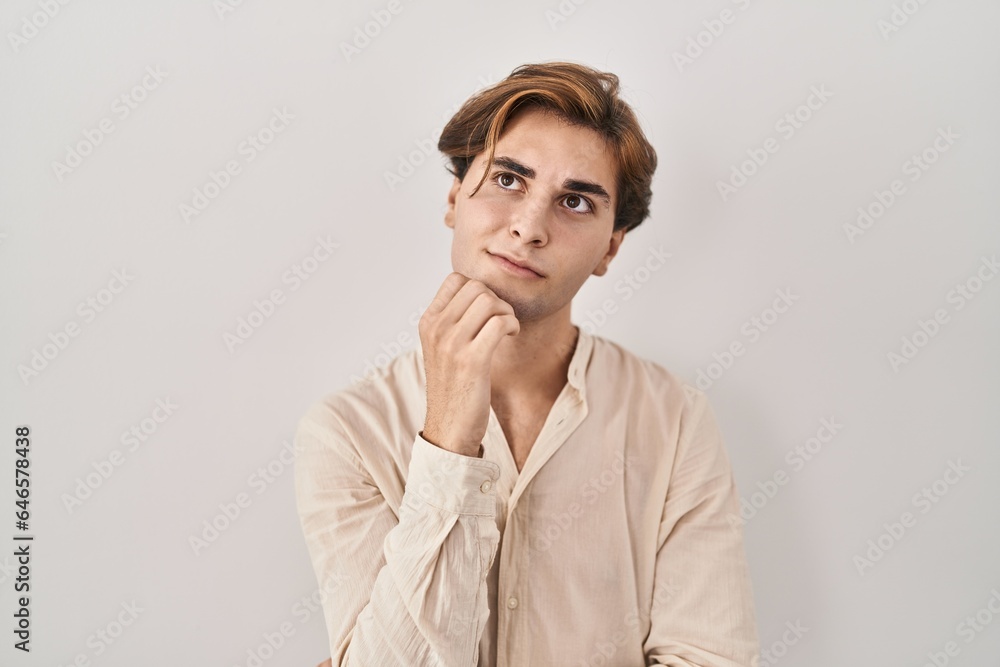 Young man standing over isolated background with hand on chin thinking about question, pensive expression. smiling with thoughtful face. doubt concept. Young man standing over isolated background with hand on chin thinking about question, pensive expression. smiling with thoughtful face. doubt concept.
