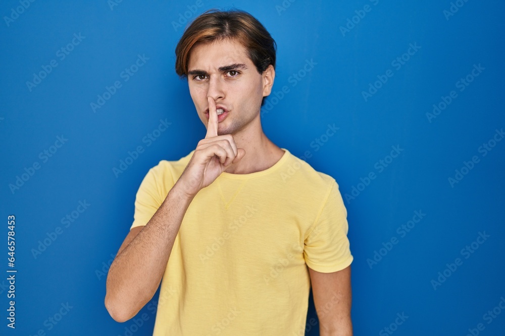 Young man standing over blue background asking to be quiet with finger on lips. silence and secret concept. Young man standing over blue background asking to be quiet with finger on lips. silence and secret concept.