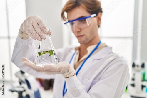 Young caucasian man scientist holding test tube with plant at laboratory