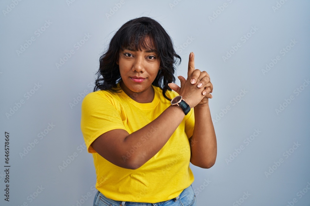 Hispanic woman standing over blue background holding symbolic gun with hand gesture, playing killing shooting weapons, angry face Hispanic woman standing over blue background holding symbolic gun with hand gesture, playing killing shooting weapons, angry face