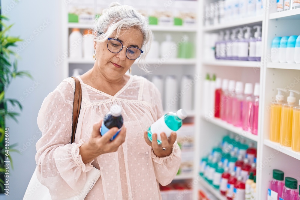 Middle age grey-haired woman customer smiling confident holding medication bottles at pharmacy