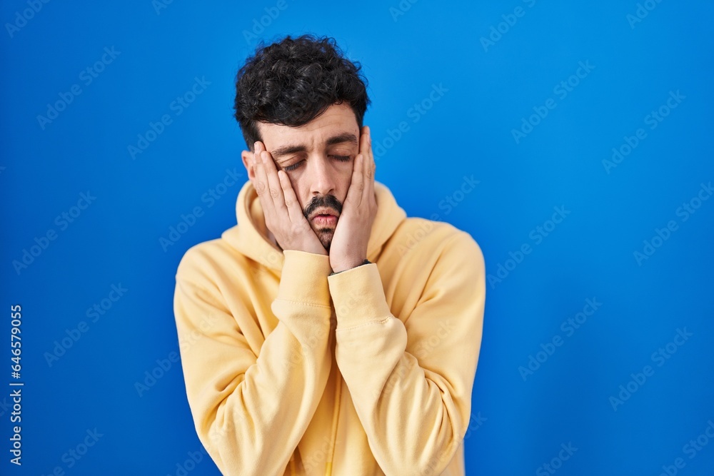 Hispanic man standing over blue background tired hands covering face, depression and sadness, upset and irritated for problem