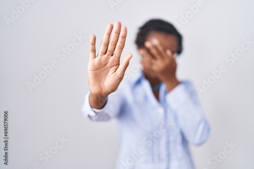 African woman with dreadlocks standing over white background wearing glasses covering eyes with hands and doing stop gesture with sad and fear expression. embarrassed and negative concept.