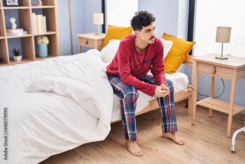 Young caucasian man sitting on bed with serious expression at bedroom