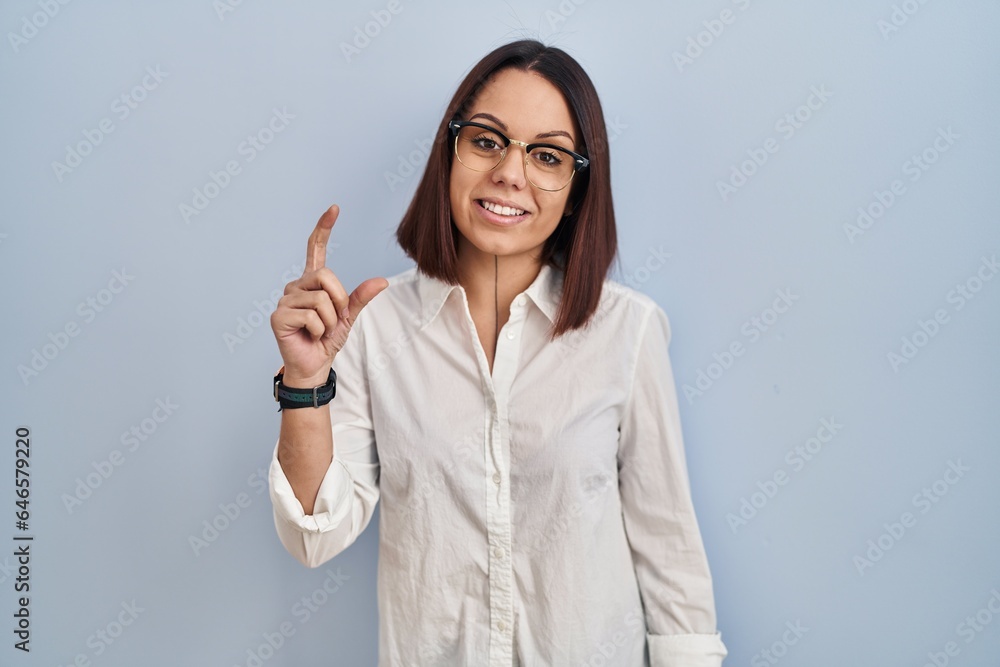 Young hispanic woman standing over white background smiling and confident gesturing with hand doing small size sign with fingers looking and the camera. measure concept. Young hispanic woman standing over white background smiling and confident gesturing with hand doing small size sign with fingers looking and the camera. measure concept.