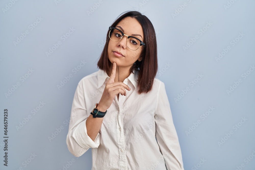 Young hispanic woman standing over white background thinking concentrated about doubt with finger on chin and looking up wondering Young hispanic woman standing over white background thinking concentrated about doubt with finger on chin and looking up wondering