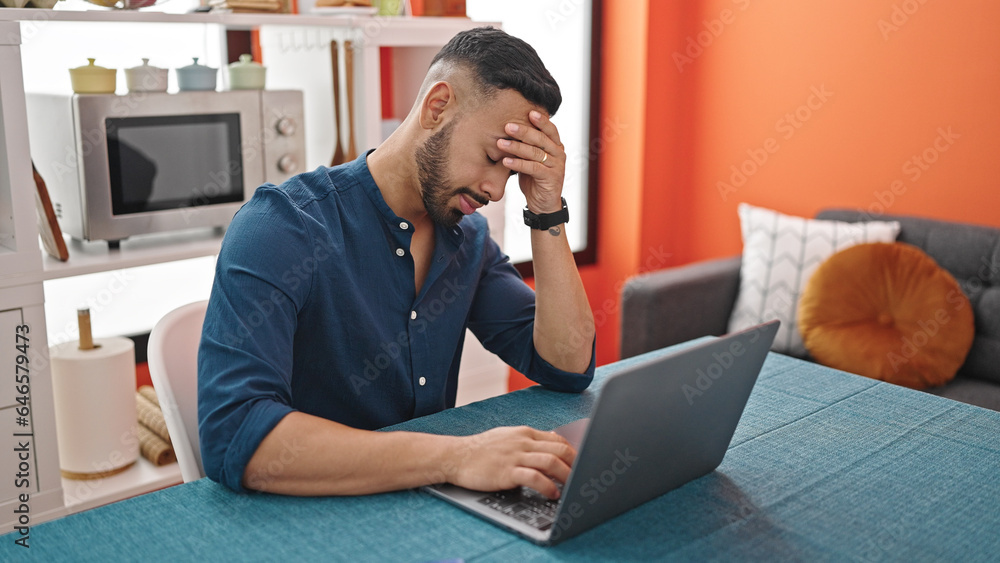 Young hispanic man stressed using laptop sitting on the table at dinning room Young hispanic man stressed using laptop sitting on the table at dinning room