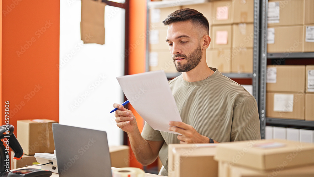 Young hispanic man ecommerce business using laptop reading document at office Young hispanic man ecommerce business using laptop reading document at office