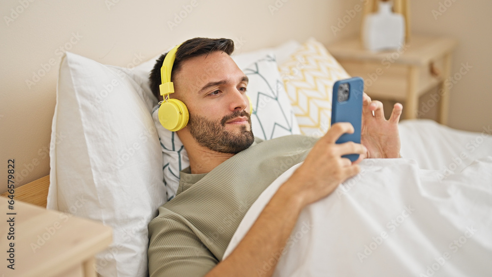 Obraz premium Young hispanic man listening to music lying on bed at bedroom